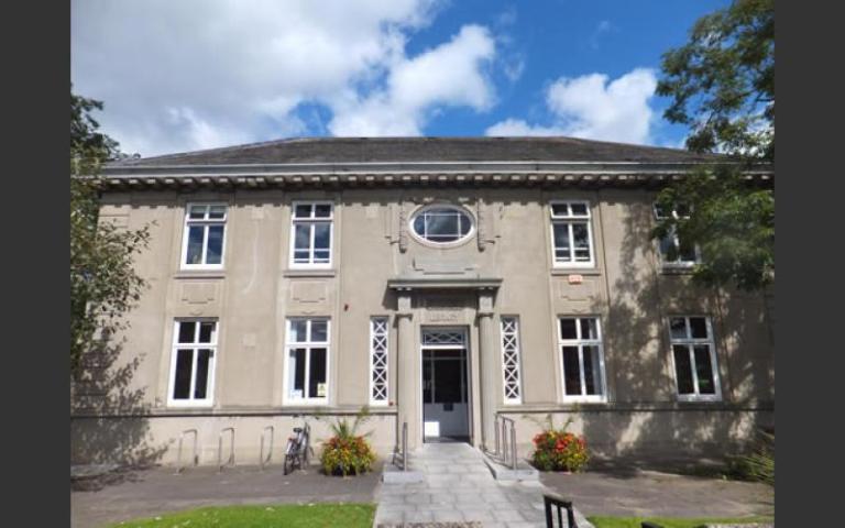 An image of Dundrum library. It is a Carnegie building in a sandy grey colour. It's a sunny day with blue skies visible behind the building.